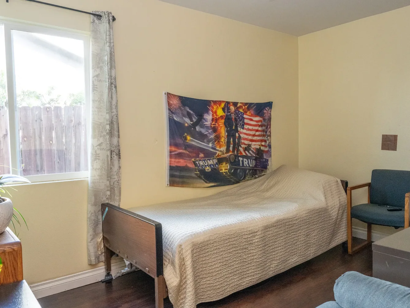 Bright resident bedroom featuring adjustable hospital bed, comfortable seating, and large window