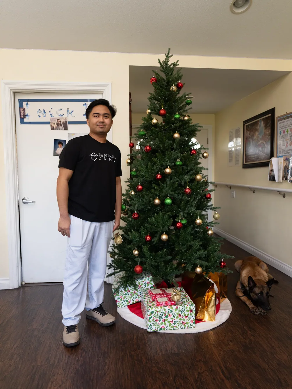 Caregiver standing beside decorated Christmas tree in warm residential care home living room
